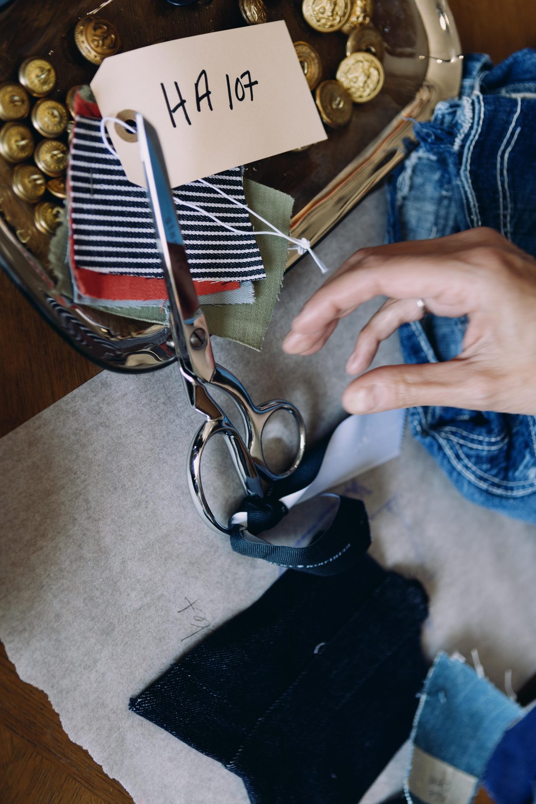 Swatches, brass military buttons and worn denim on the studio table