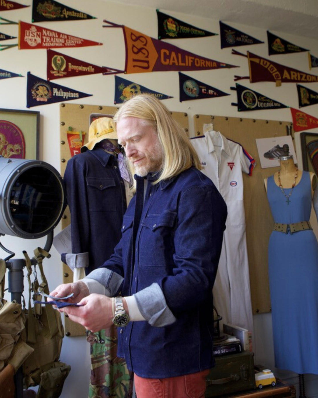 Man in a blue jacket using a smartphone in a room with vintage flags and clothing.