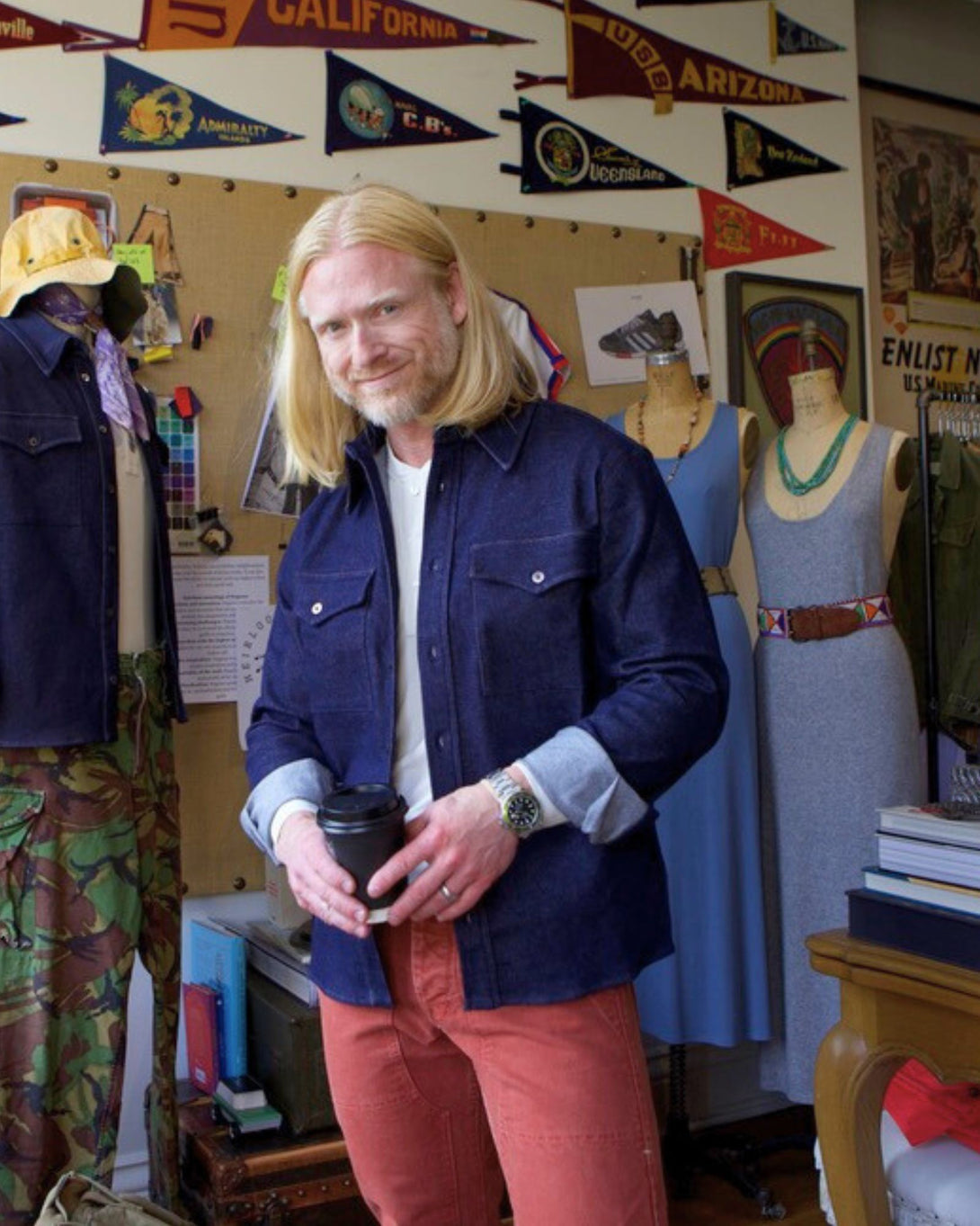 Man holding a cup in a room with vintage flags and clothing