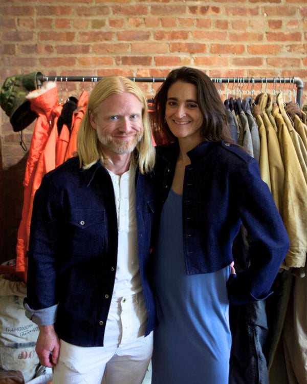 Two people standing in a clothing store with racks of jackets behind them.
